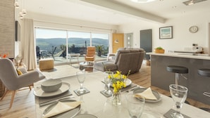 A modern dining area with a table set for four, a bar area, and a large window offering a view of the countryside. - Vikings Annexe, Minehead (Minehead)