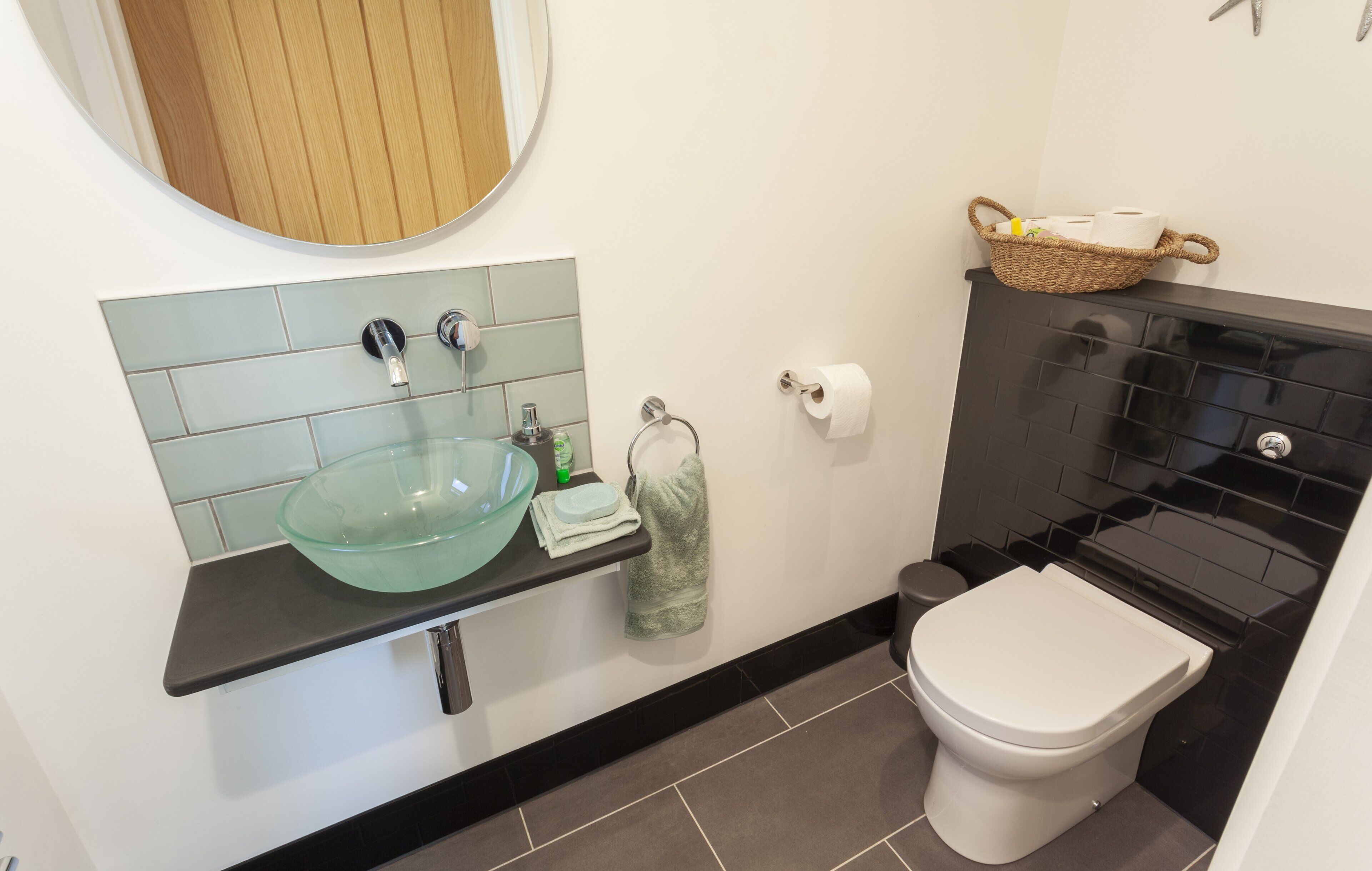 Une salle de bain avec un lavabo en forme de bol en verre, des toilettes et une douche carrelée de carreaux noirs.