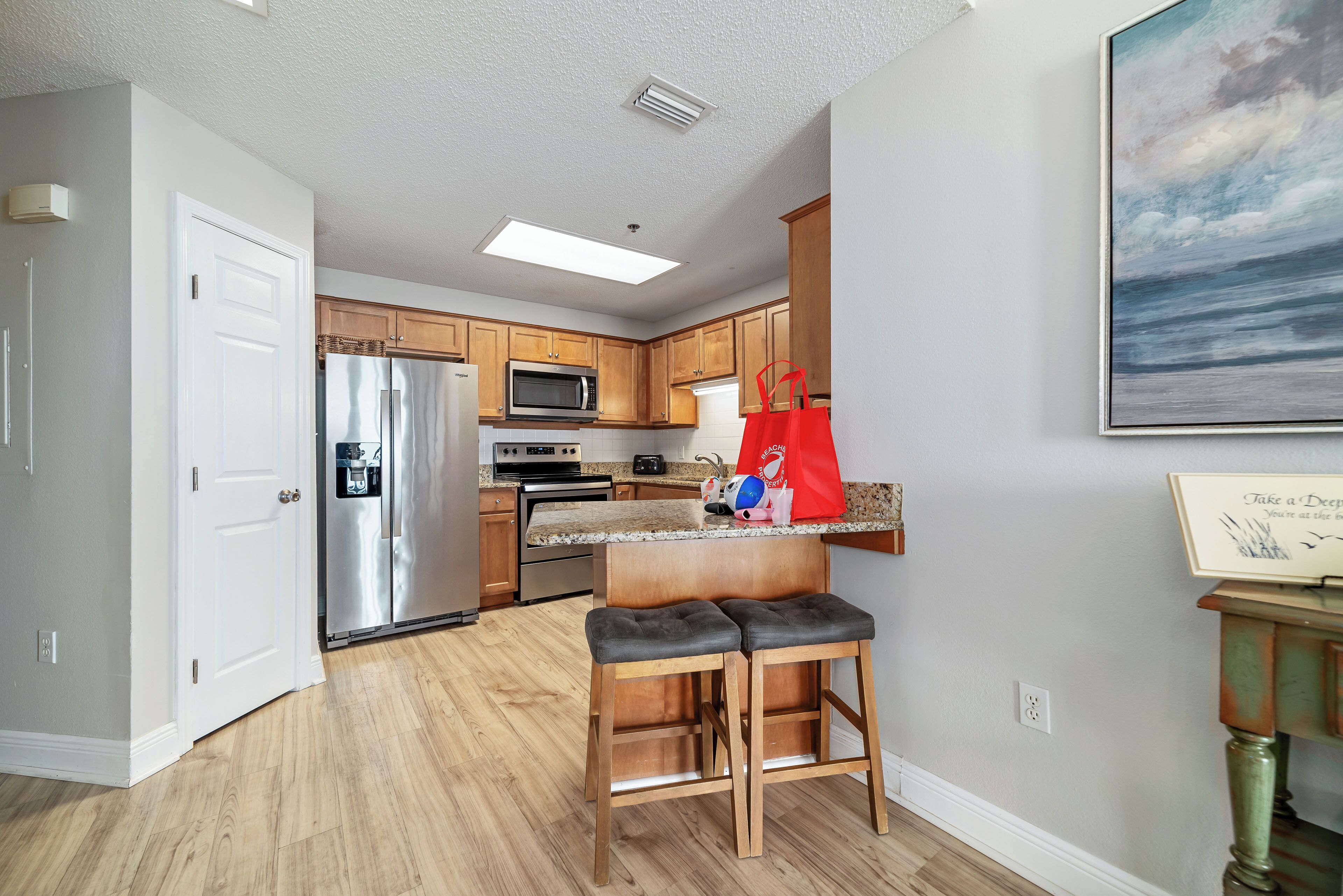 A modern kitchen with wooden cabinets, stainless steel appliances, and a bar stool area.