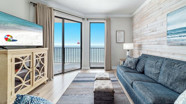 A living room with a large TV, a blue sofa, a wooden cabinet, and a view of the ocean through the sliding doors. - LUXURY PHOENIX UNIT, GREAT FOR FAMILIES, TONS OF AMENTIES (Orange Beach)