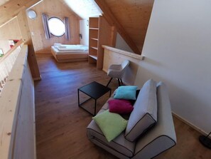 Quarto estilo loft com piso de madeira, um sofá com almofadas, uma mesa pequena, uma cadeira e uma cama com janela.