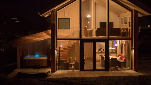 Een modern huis met een glazen gevel, een jacuzzi en een trap naar de bovenverdieping.