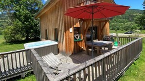 Een houten chalet met terras, een jacuzzi en een rode parasol.