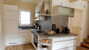 Een kleine keuken met witte kasten, een inbouwoven, een magnetron en een klein aanrecht met een koffiezetapparaat en broodrooster.