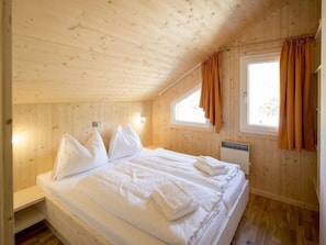 A wooden cabin bedroom with a bed, pillows, and a window with curtains.