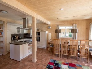 A spacious kitchen with white cabinets and a central island, a dining area with wooden chairs and a colorful rug, and a large window with curtains.