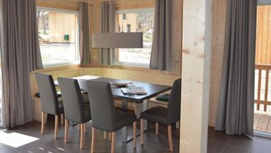 A dining area with a table and chairs, wooden walls, and large windows with curtains. - mit 4 Schlafzimmern & IR-Sauna by Interhome (Sankt Georgen am Kreischberg)