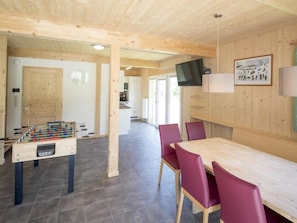 A wooden interior with a foosball table, a dining area with red chairs, and a TV mounted on the wall.