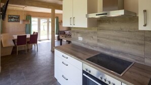 A modern kitchen with wooden cabinets, a built-in stove, and a dining area with a table and chairs. - mit 4 Schlafzimmern & IR-Sauna by Interhome (Sankt Georgen am Kreischberg)