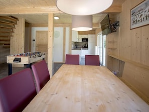 A wooden interior with a foosball table, a dining table, and red chairs.