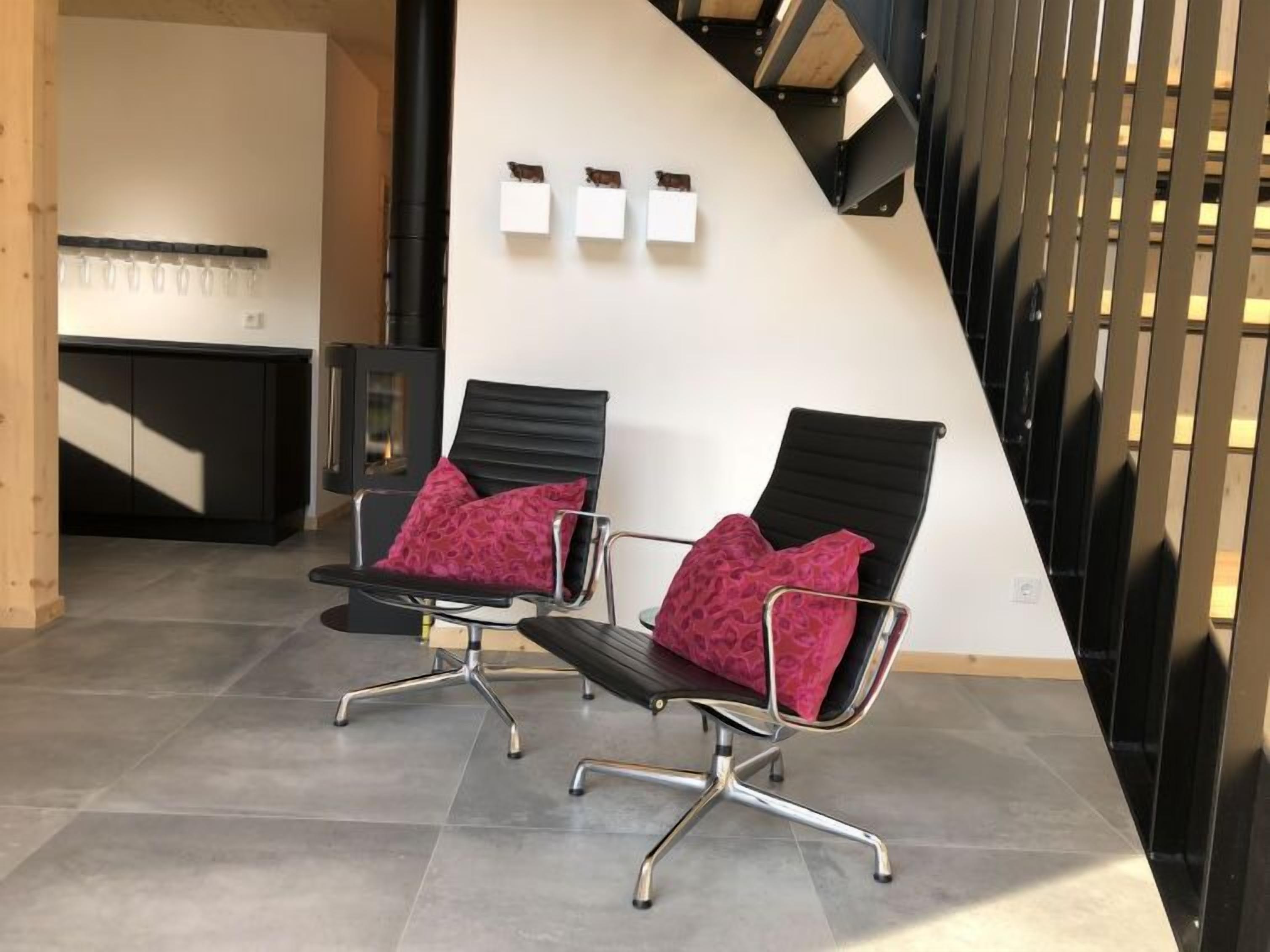 Un intérieur moderne avec deux chaises noires dotées de coussins rouges, un meuble noir et un mur incurvé orné de trois éléments décoratifs carrés blancs.