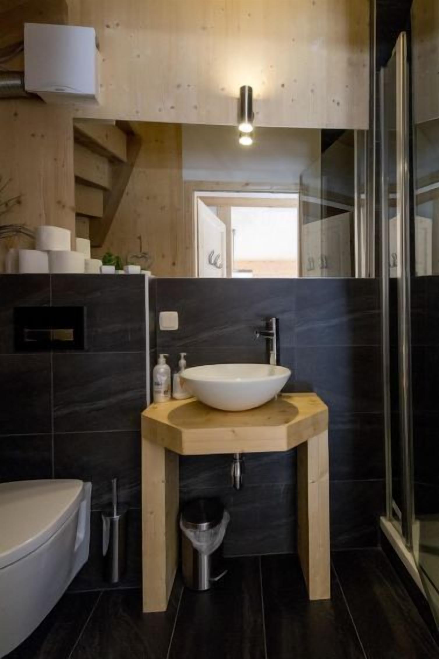 Un baño moderno con lavamanos independiente, baldosas oscuras y mampara de vidrio.