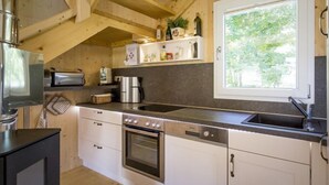 Una cocina compacta con vigas de madera, horno empotrado, cafetera y ventana con vista a la vegetación.