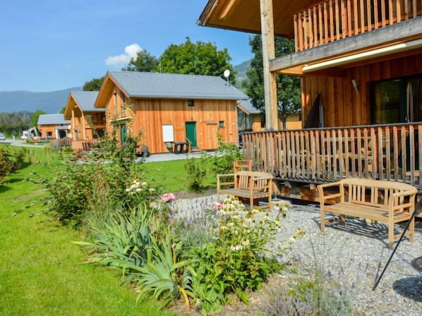 A wooden cabin with a balcony, surrounded by a garden with various plants and flowers.