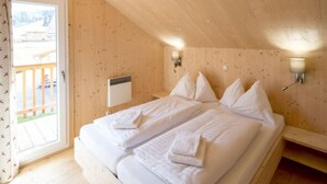 Un dormitorio de cabaña de madera con una cama doble, dos mesitas de noche, una ventana con cortinas y un calentador fijado a la pared.