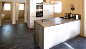 A modern kitchen with a central island, white cabinetry, and a dark tiled floor. - Premium mit 5 SZ, Sauna oder IR-Sauna by Interhome (Sankt Georgen am Kreischberg)