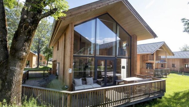 A modern wooden cabin with large glass windows, a deck, and a surrounding grassy area. - Premium mit 5 SZ, Sauna oder IR-Sauna by Interhome (Sankt Georgen am Kreischberg)