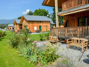 A wooden cabin with a balcony, surrounded by a garden with various plants and flowers.