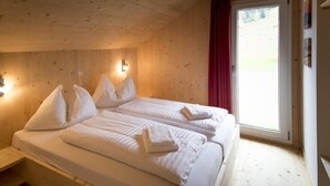 Un dormitorio de cabaña de madera con dos camas, una ventana con cortina roja y una lámpara fijada a la pared.