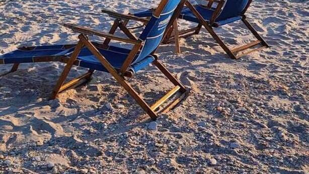 Two beach chairs with a yellow umbrella on a sandy beach with the ocean in the background.