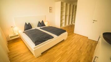 Une chambre avec un lit double, des tables de chevet, une étagère murale et une porte donnant sur une autre pièce.