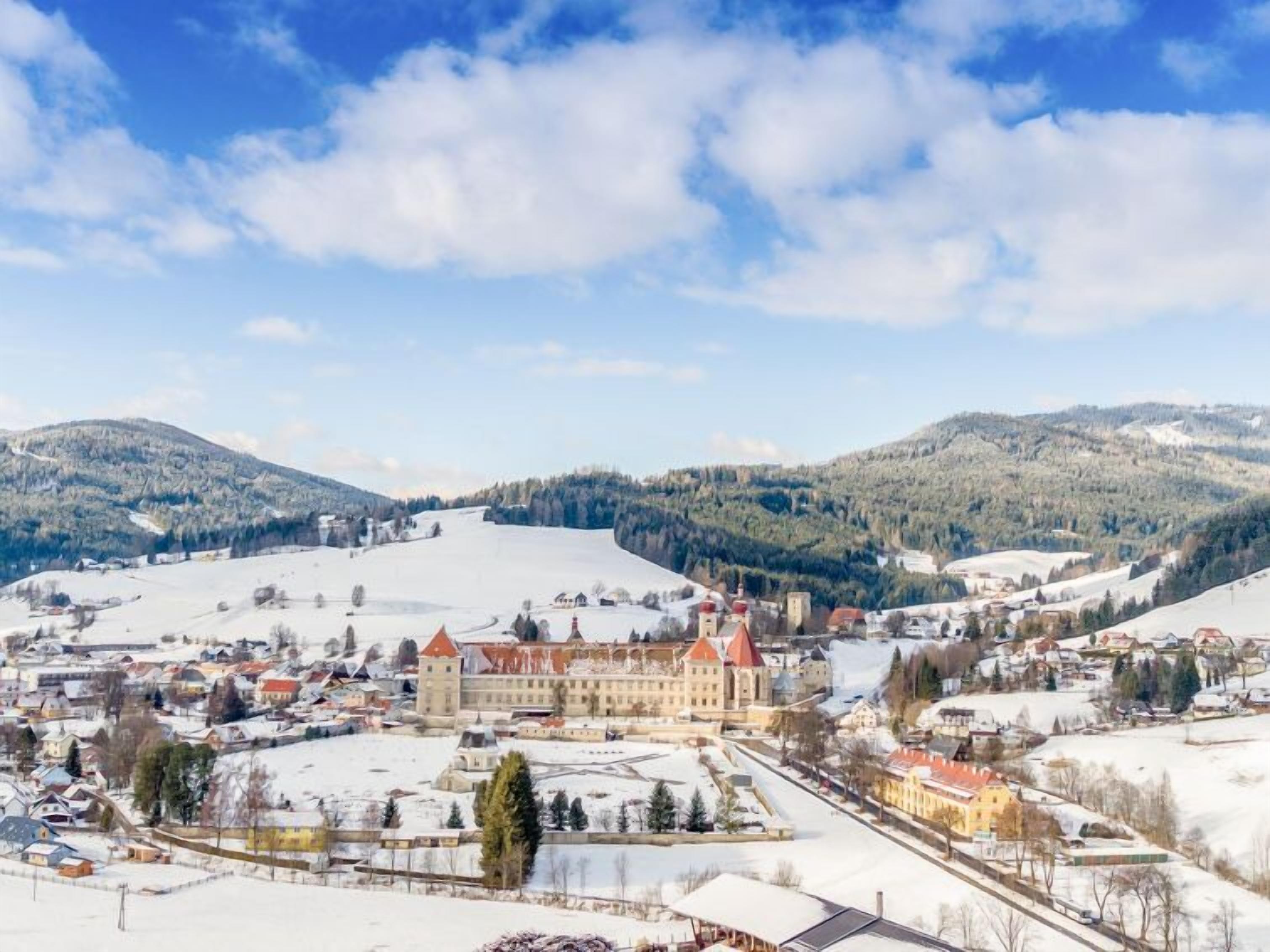 Una cittadina storica con un imponente edificio simile a un castello, circondata da colline innevate e un cielo sereno.