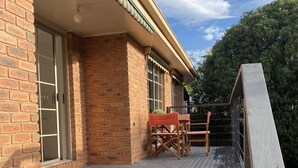 Eine Holzdar Terrasse mit Metallgeländer, ein Backsteinhaus mit einem Fenster und ein Tisch mit Stühlen.