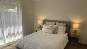 Ein ordentlich bezogenes Bett mit einem gemusterten Überwurf, zwei Nachttische mit Lampen und durchscheinende Vorhänge an einem Fenster.