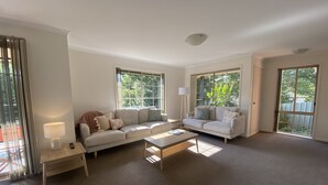 Ein geräumiges Wohnzimmer mit zwei Sofas, einem Couchtisch und einer Lampe. Große Fenster sorgen für natürliches Licht und Blick ins Grüne.