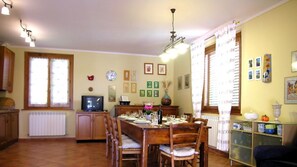 A dining area with a wooden table set for four, a television on a cabinet, and a radiator below a window.