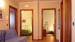 Een gang die leidt naar een slaapkamer met een bed, nachtkastje en kledingrek.