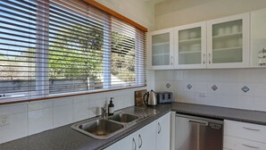 A modern kitchen with a granite countertop, stainless steel appliances, and white cabinetry. - Cordova - Perfect Summer or Winter Getaway (Merimbula)