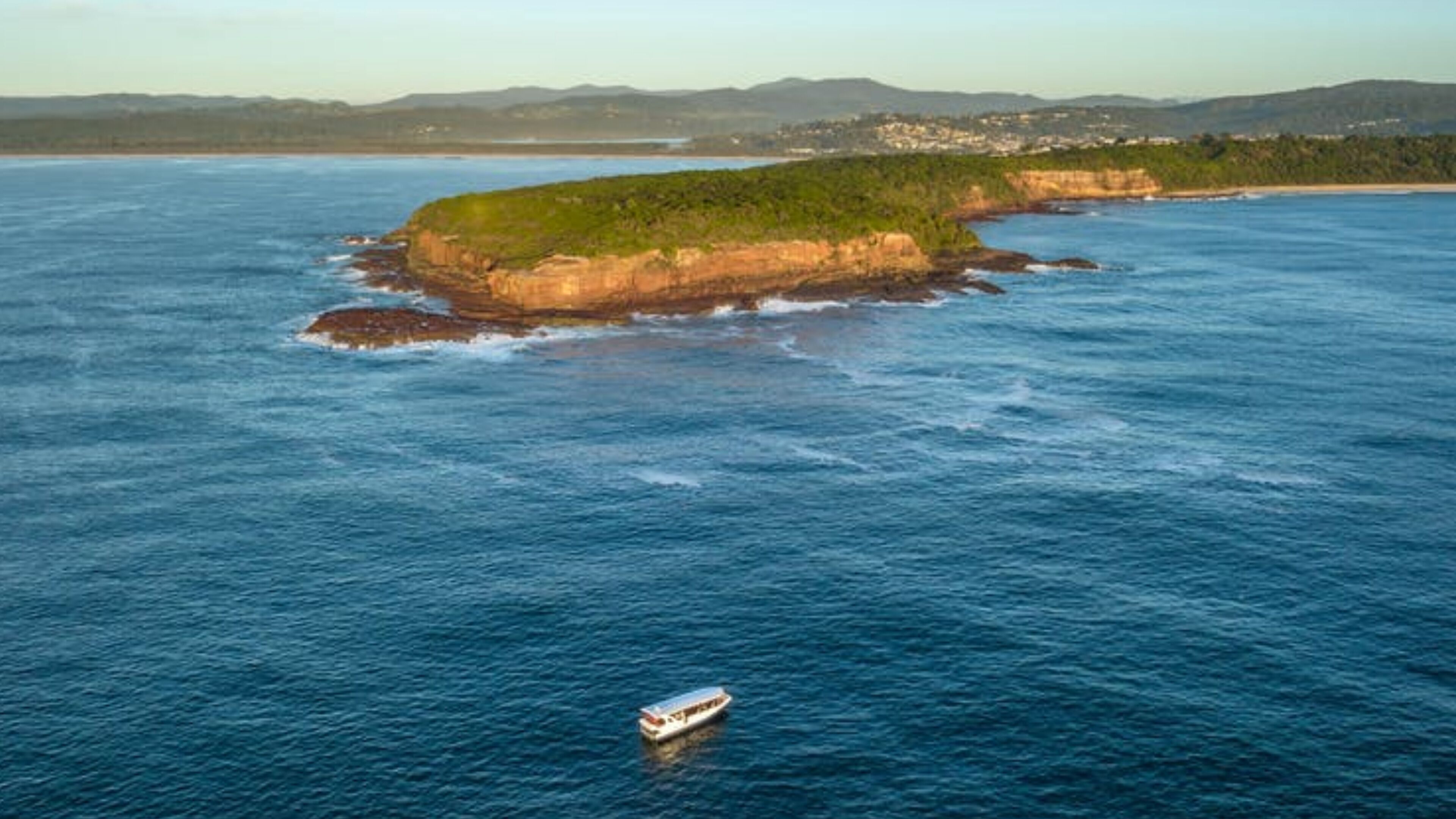 A coastal landscape with a small island and a boat in the water.