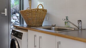 A kitchen with a washing machine, a stainless steel sink, and a wicker basket on the countertop. - Cordova - Perfect Summer or Winter Getaway (Merimbula)