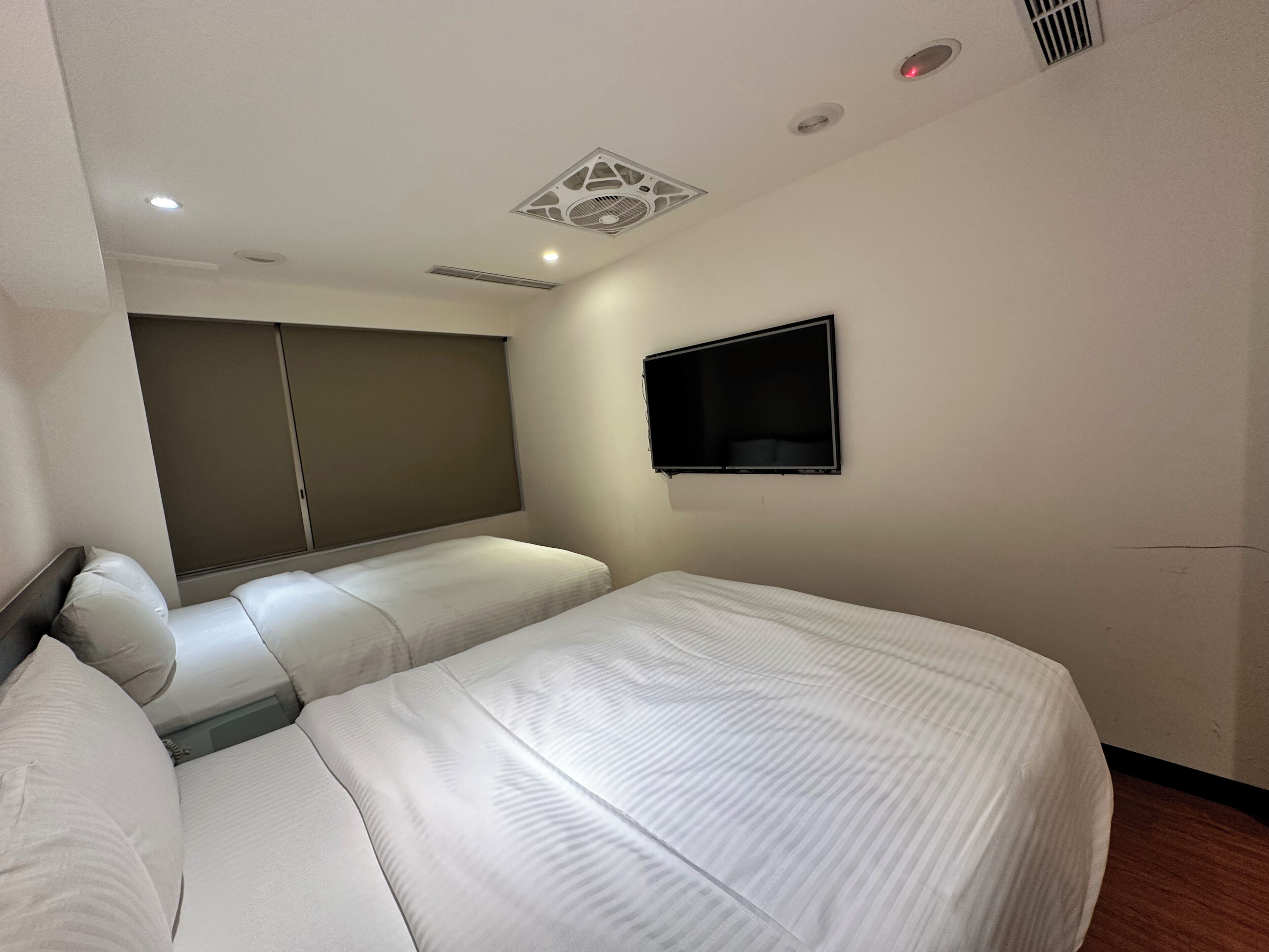 Une chambre d’hôtel avec deux lits, un téléviseur fixé au mur et un ventilateur de plafond.