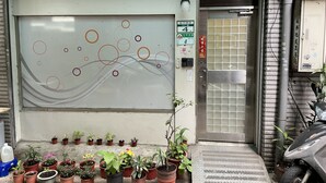 A building entrance with a closed door, a sign with numbers, and potted plants outside. - Good Day Inn (Taipei)