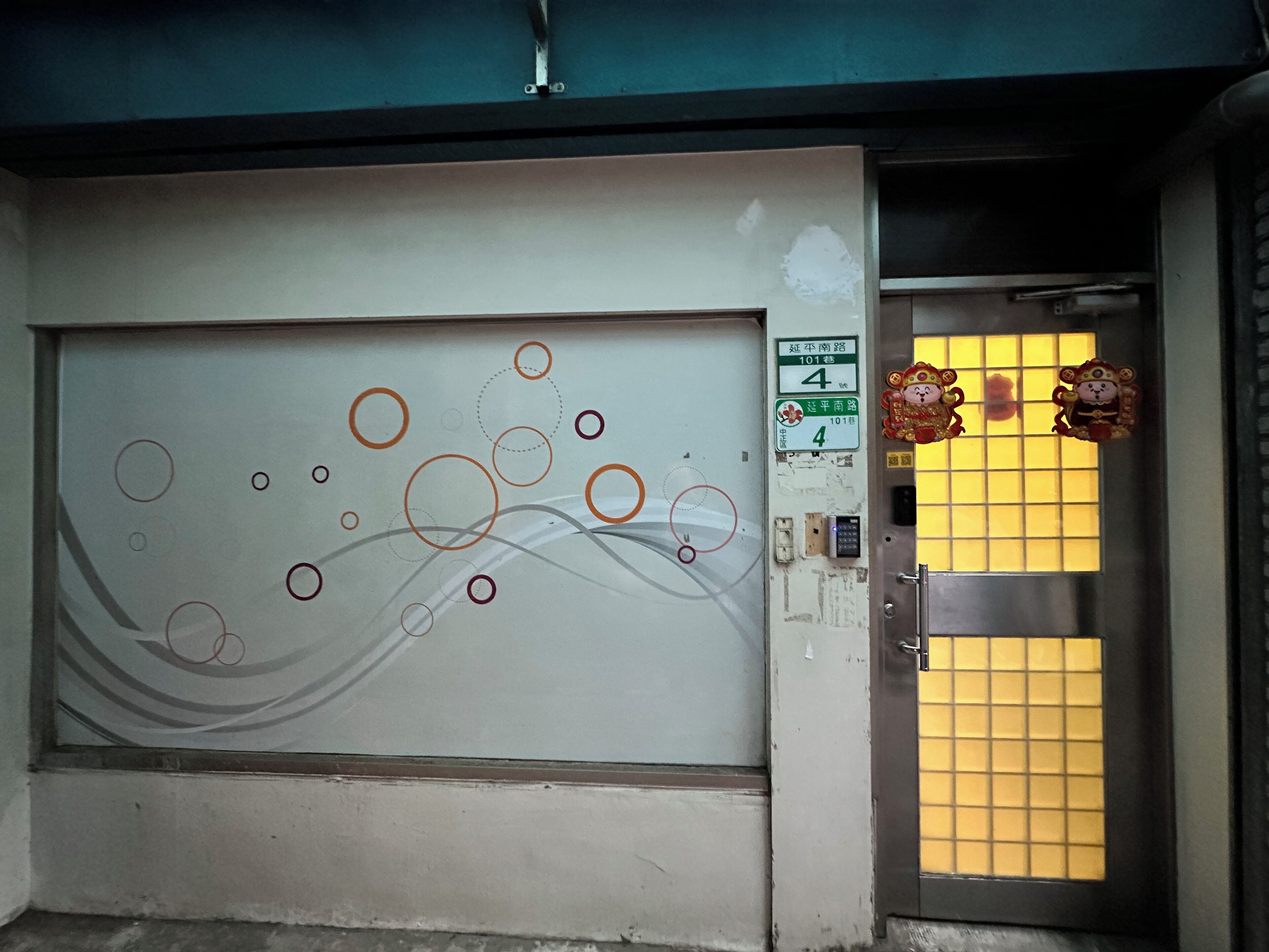 A door with a decorative panel featuring abstract circles and lines, a sign with numbers and text, and a window with a grid pattern.