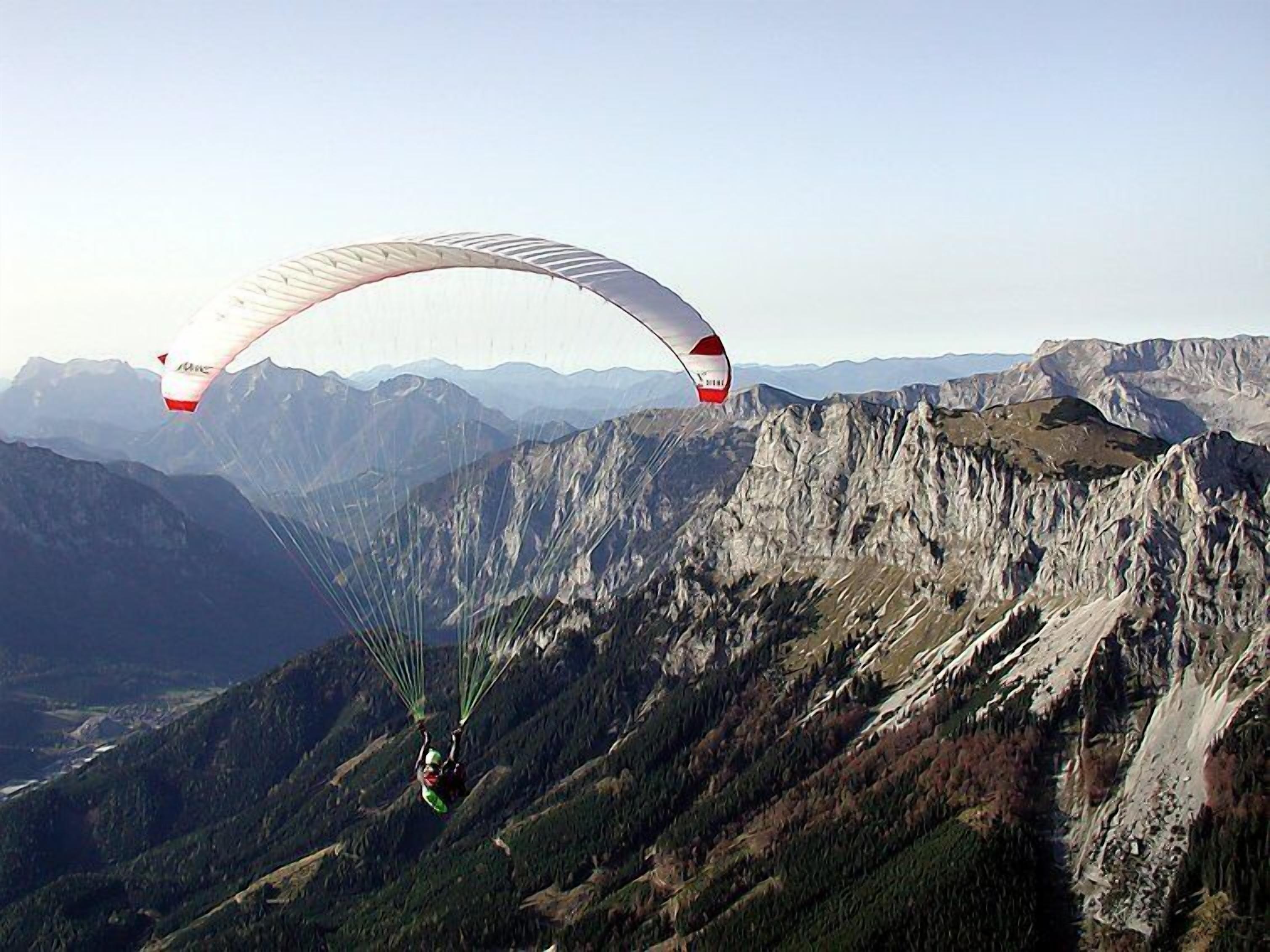 A paraglider in mid-flight over a mountainous landscape.