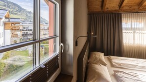 Une chambre d’hôtel avec une grande fenêtre, un lit, un radiateur et une vue sur des immeubles et des collines.