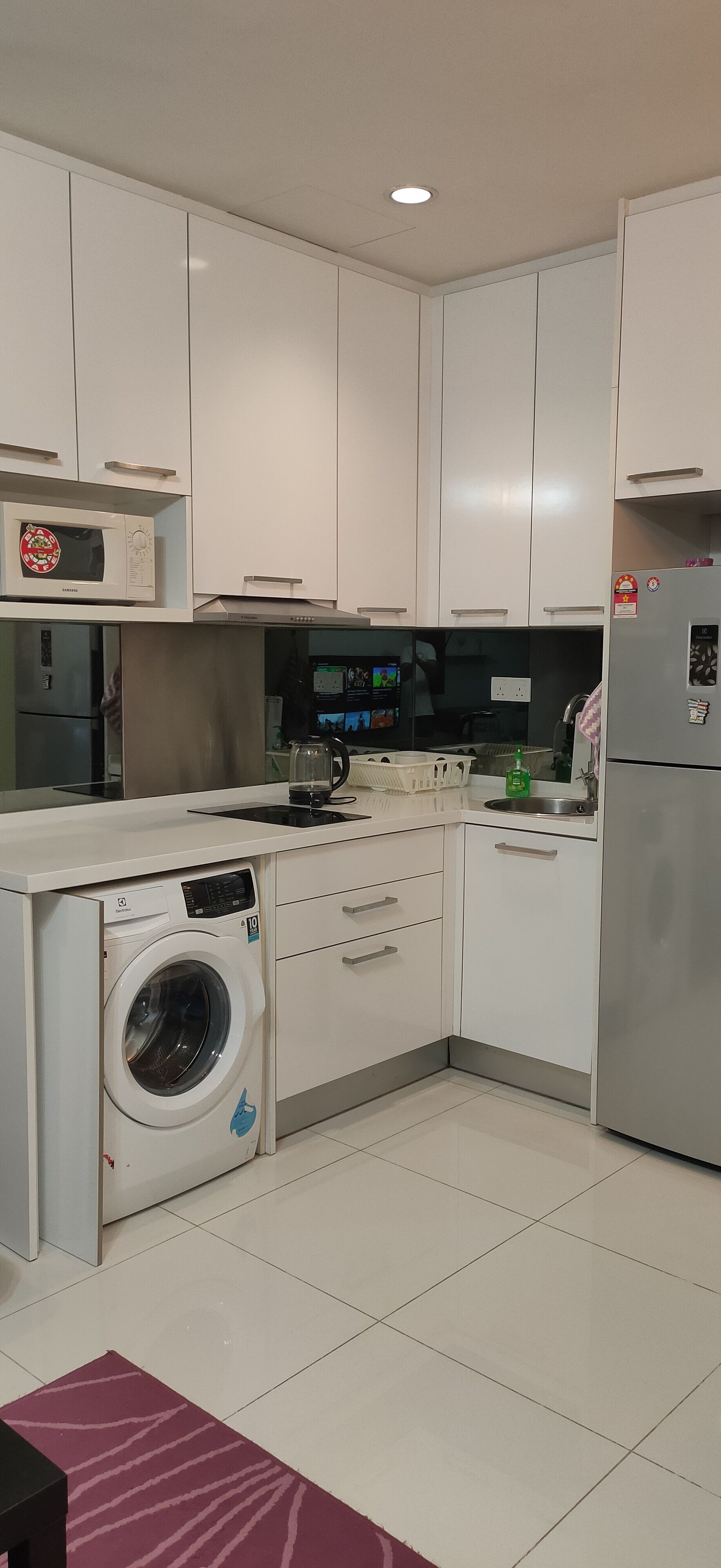 A modern kitchen with white cabinets, a built-in microwave, a washing machine, and a refrigerator.