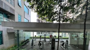 Un espace de remise en forme en plein air, équipé de divers appareils d’exercice, entouré de murs de verre et offrant une vue sur le paysage urbain.