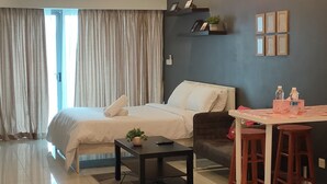 Une chambre d’hôtel moderne comprenant un lit, un coin repas avec une table et des chaises, un ventilateur de plafond et une grande fenêtre avec des rideaux.