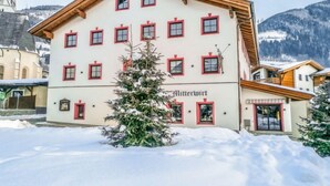 Ein mehrstöckiges Gebäude mit verschneitem Vorfeld und einem Weihnachtsbaum davor.