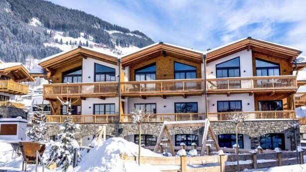 Ein mehrstöckiges Hotel mit hölzernen Balkonen und großen Fenstern vor einer verschneiten Bergkulisse.