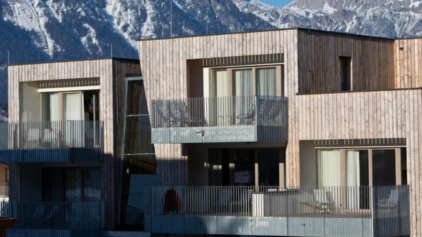 Un edificio moderno in legno con balconi, ampie finestre e montagne sullo sfondo.