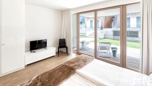 Una camera da letto moderna con un letto grande, una TV, un'area salotto con una poltrona e una porta scorrevole in vetro che dà su un patio esterno.