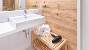 Un bagno moderno con una parete in legno decorativa, un lavandino bianco e uno scaffale in legno con asciugamani e un asciugacapelli.