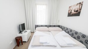Ein ordentlich eingerichtetes Schlafzimmer mit einem Bett, einem Nachttisch, einem Fernseher und einem kleinen Hocker.