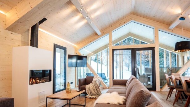 Un salon chaleureux avec une cheminée, des sièges confortables et de grandes fenêtres donnant sur l’extérieur.