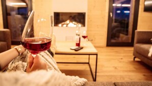 Un salon chaleureux avec une cheminée, un verre de vin rouge et un téléphone intelligent posé sur une table basse.